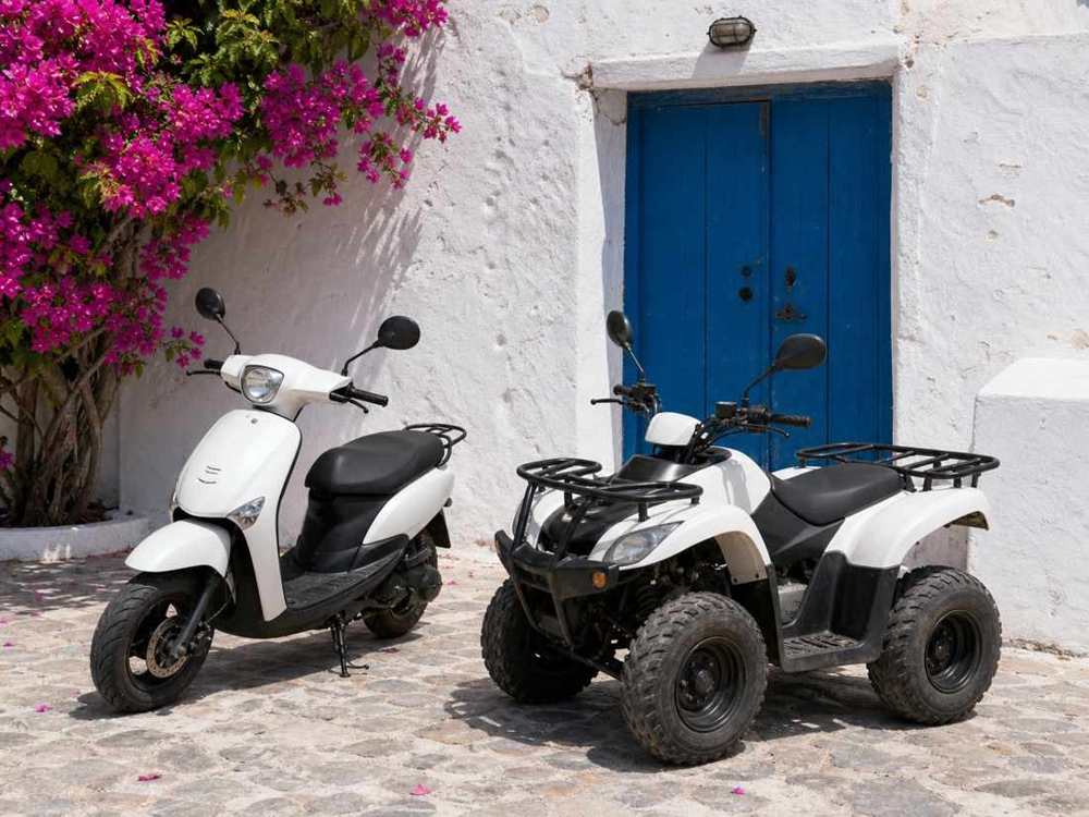 A scooter and an ATV in front of a whitewashed wall with a blue door